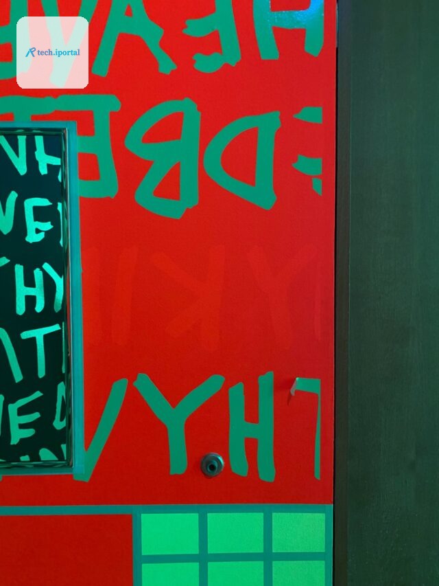 A close-up of a fluorescent mural at Newfields showing bright red DayGlo paint in an area formerly protected from light by the green vinyl lettering.