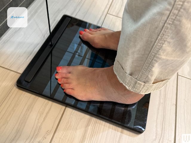 close up of a person's feet standing on a slim black scale with the scale on a tiled floor