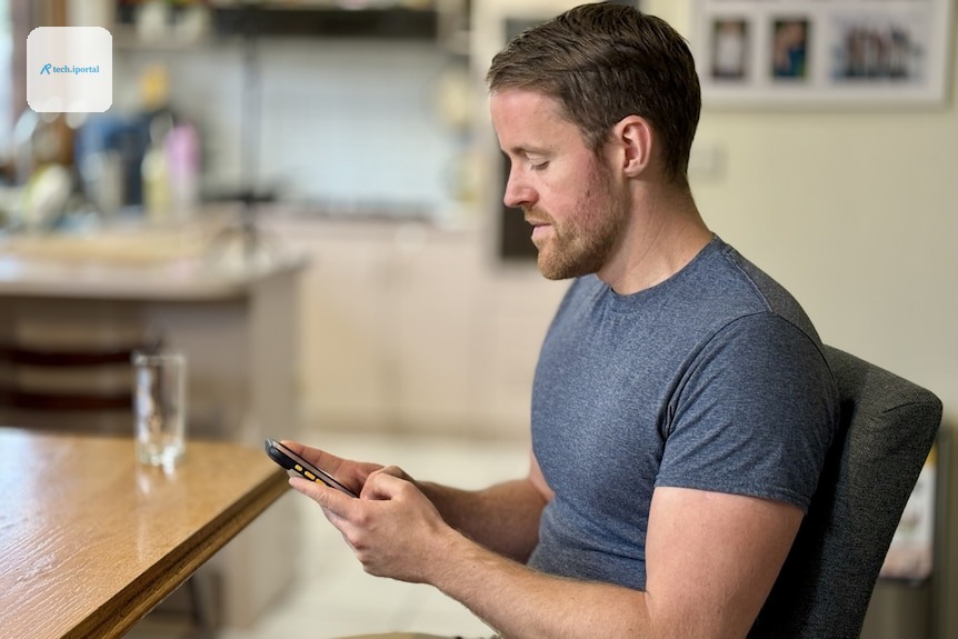 A side profile of a man in a grey t-shirt typing on a smart phone.