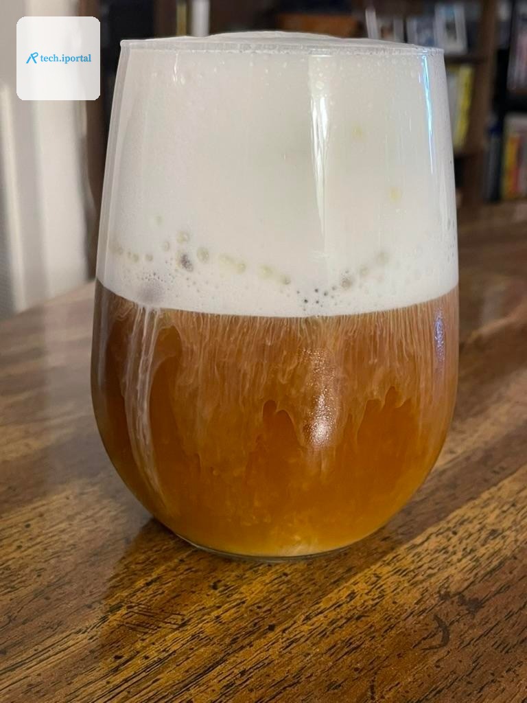 A glass of iced coffee, with a generous white foam top that’s dripping into the coffee.