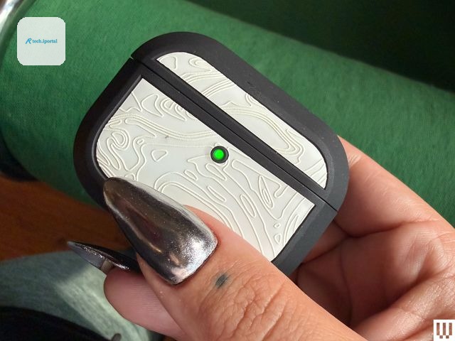 Person's hand pinching a small white case with rounded edges, black trim, and a green light turned on