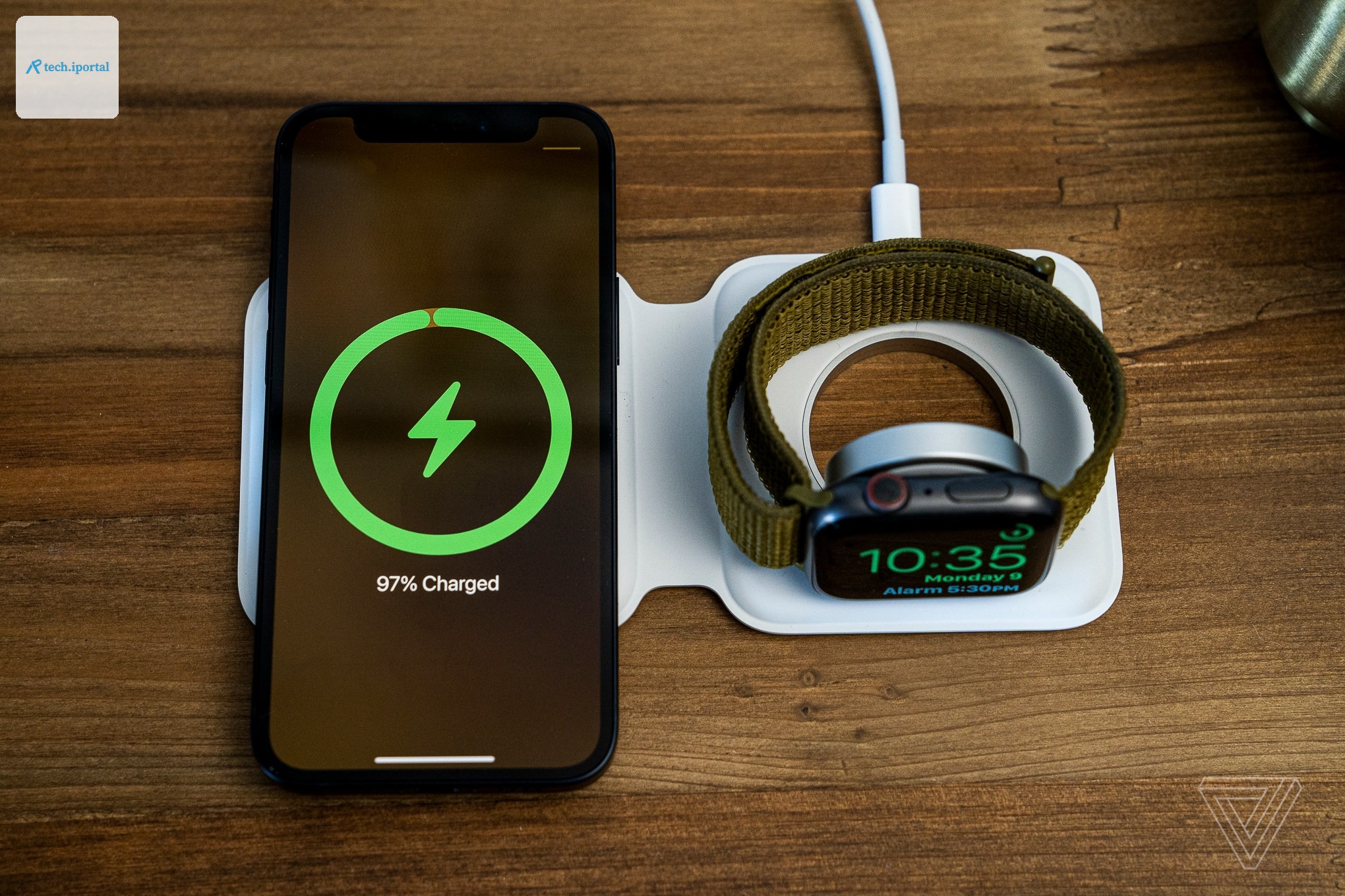 An iPhone and Apple Watch charging wirelessly on an Apple MagSafe Duo Charger, atop a wood table.