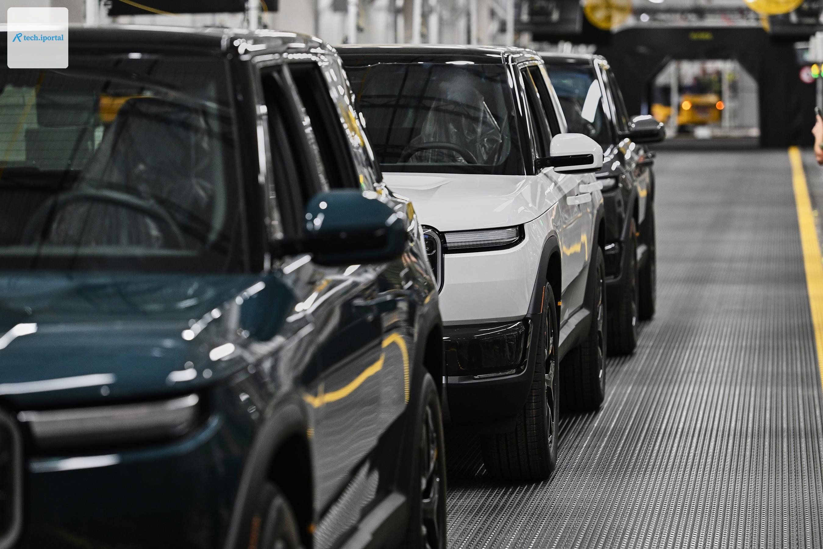 Detail of the sides of three Rivians in a line on the factory floor.