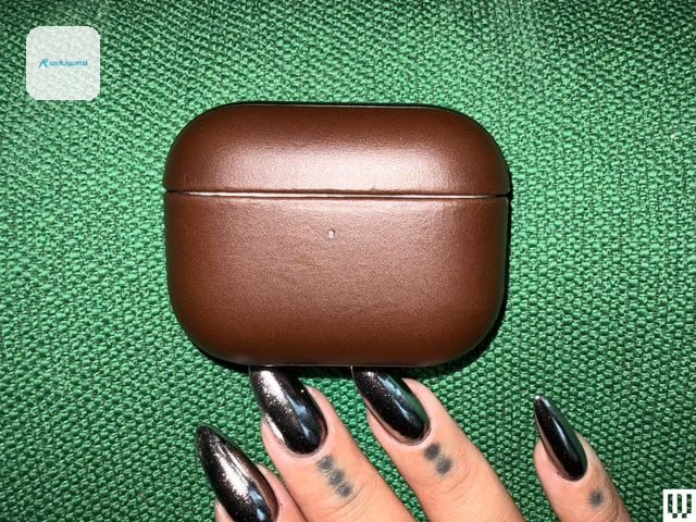 The tips of a person's fingers, with fingernails painted shiny black, beside a small leather rounded case